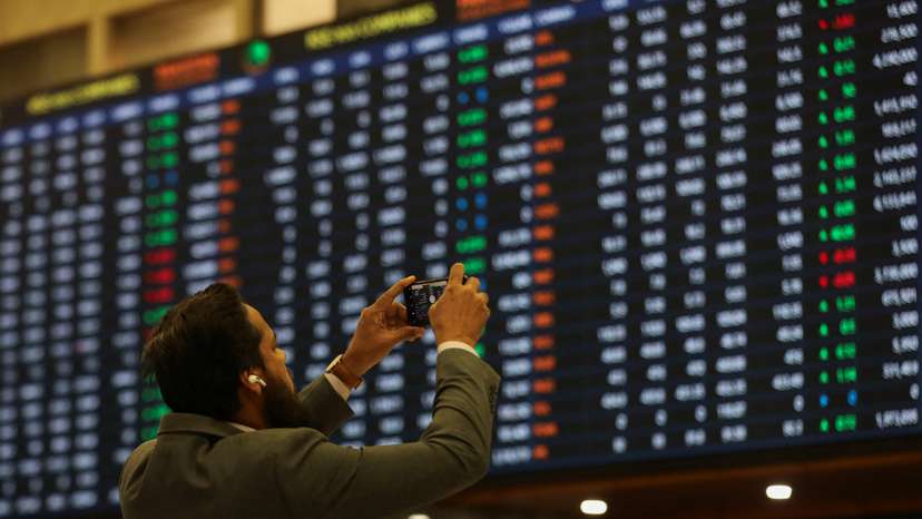 Man takes a photo of the electronic board displaying share prices during a trading session at the Pakistan Stock Exchange, in Karachi