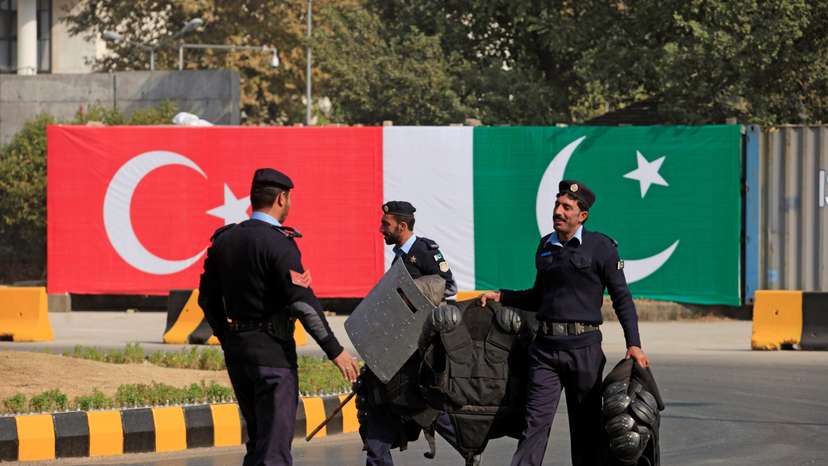 Policemen walk near the national flags of Pakistan and Turkey displayed along a road ahead of a visit of Turkish President Erdogan in Islamabad