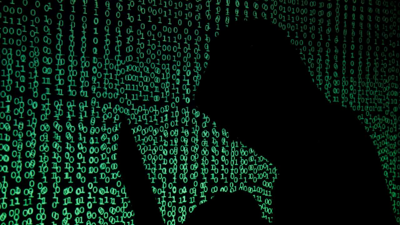 Hooded man holds laptop computer as cyber code is projected on him in this illustration picture