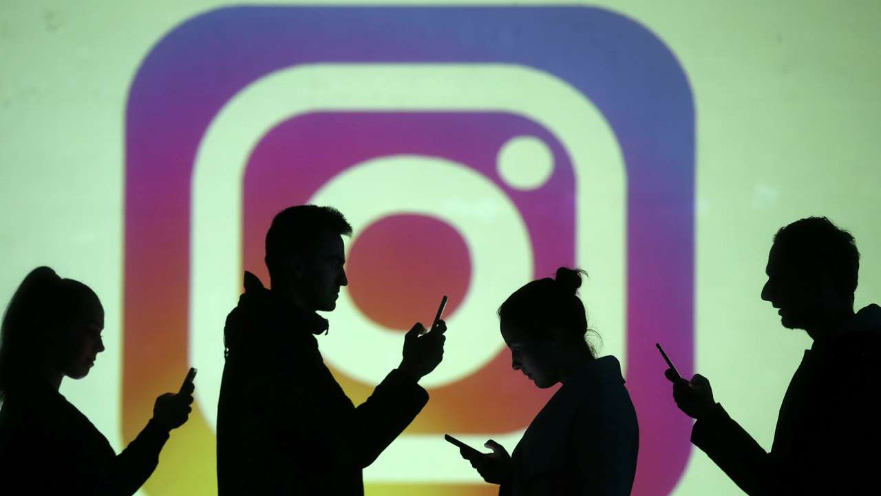 Silhouettes of mobile users are seen next to a screen projection of Instagram logo in this picture illustration