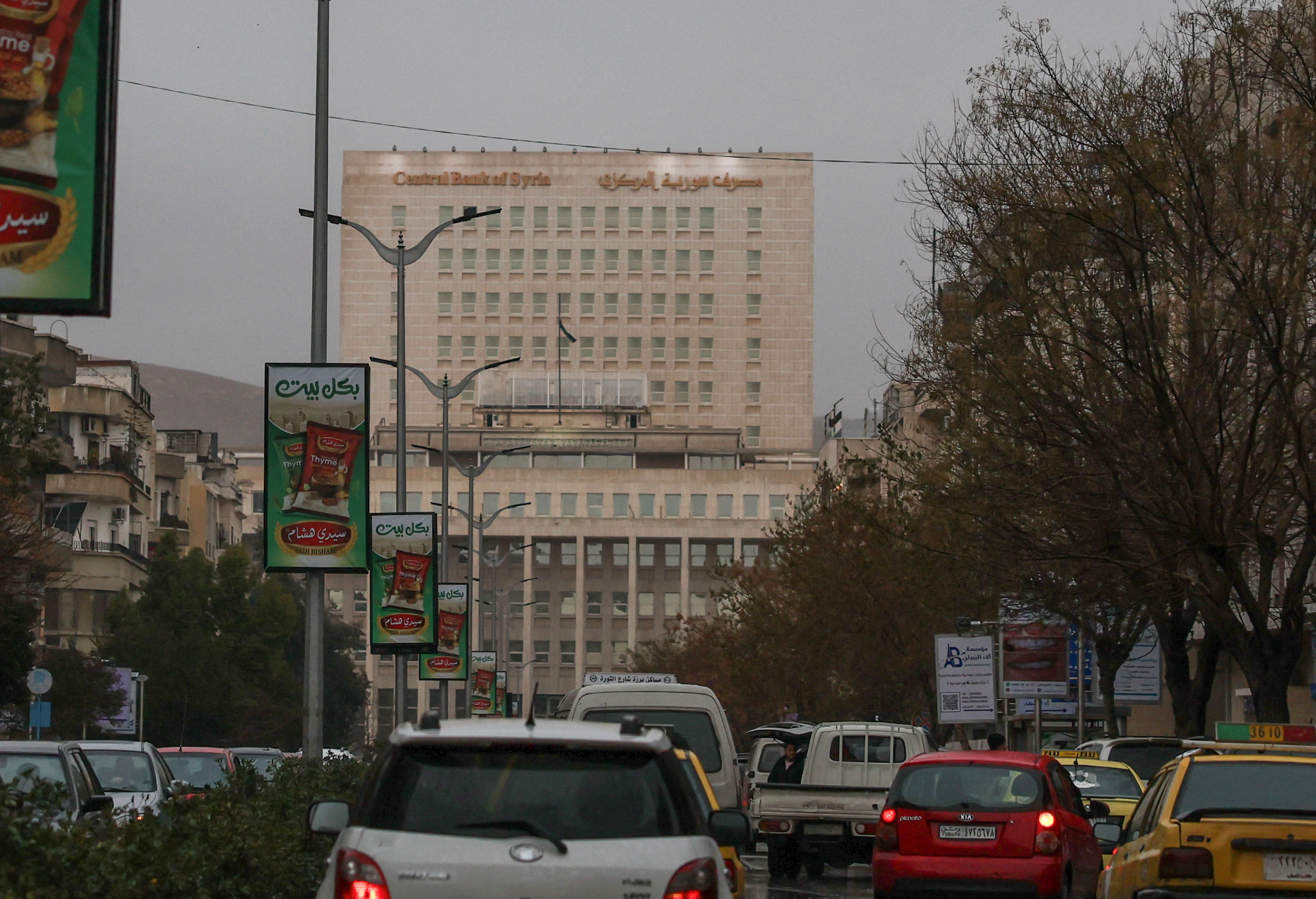 Vehicles drive as the Syrian central bank is seen in the background in Damascus