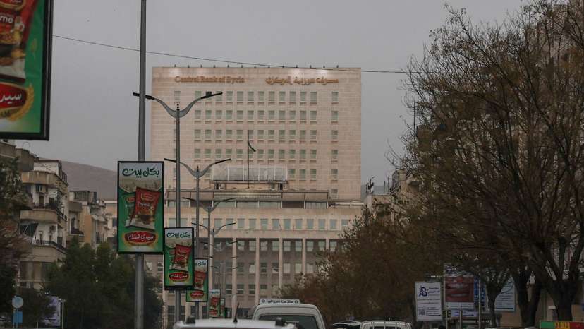 Vehicles drive as the Syrian central bank is seen in the background in Damascus
