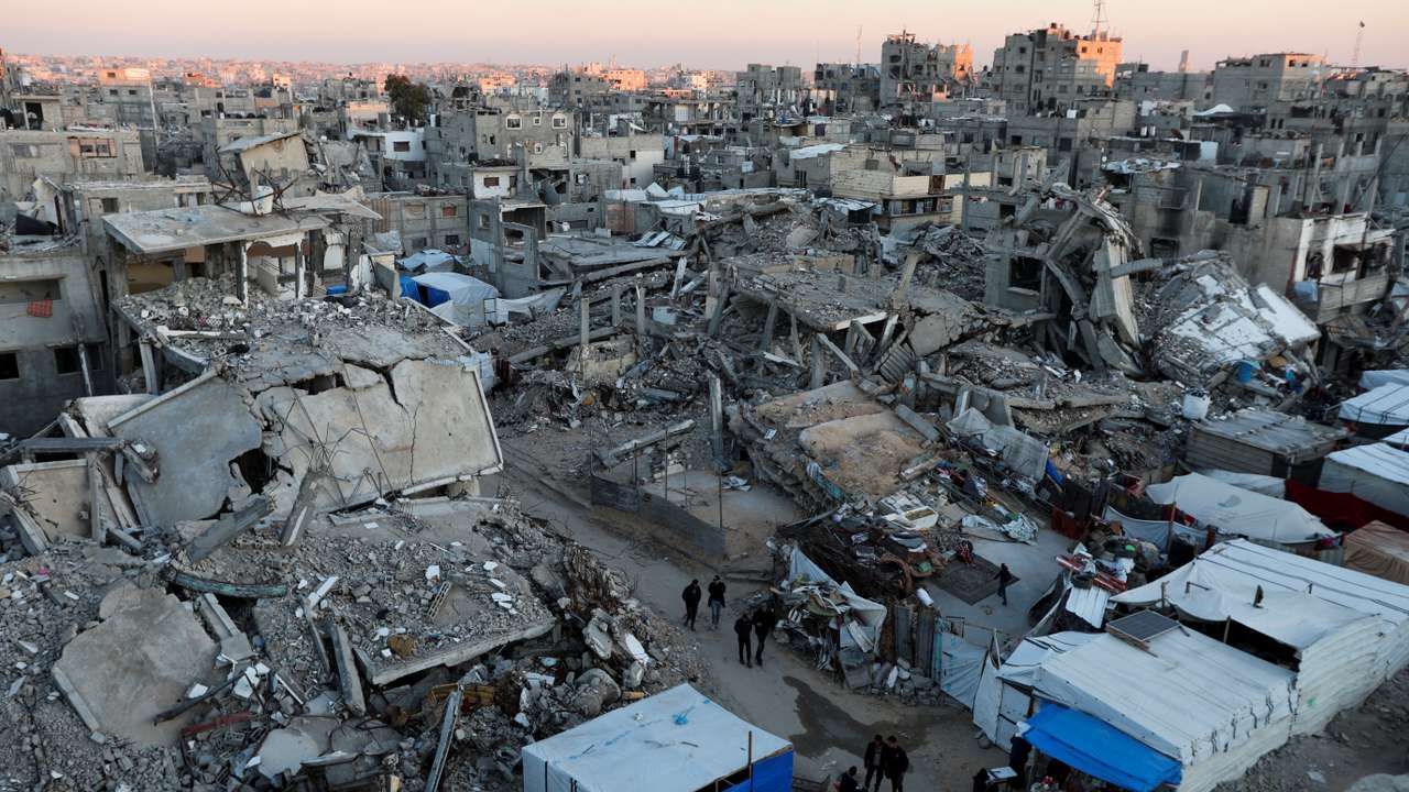 Palestinians walk past the rubble of buildings, In Khan Younis