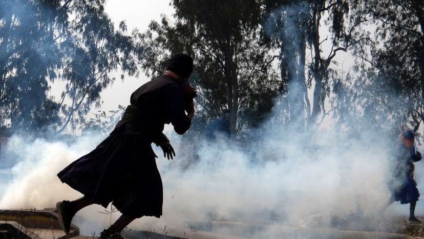 Farmers run for cover amidst tear gas smoke fired by police, at Shambhu