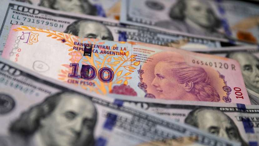 A one hundred Argentine peso bill sits on top of several one hundred U.S. dollar bills in this illustration picture