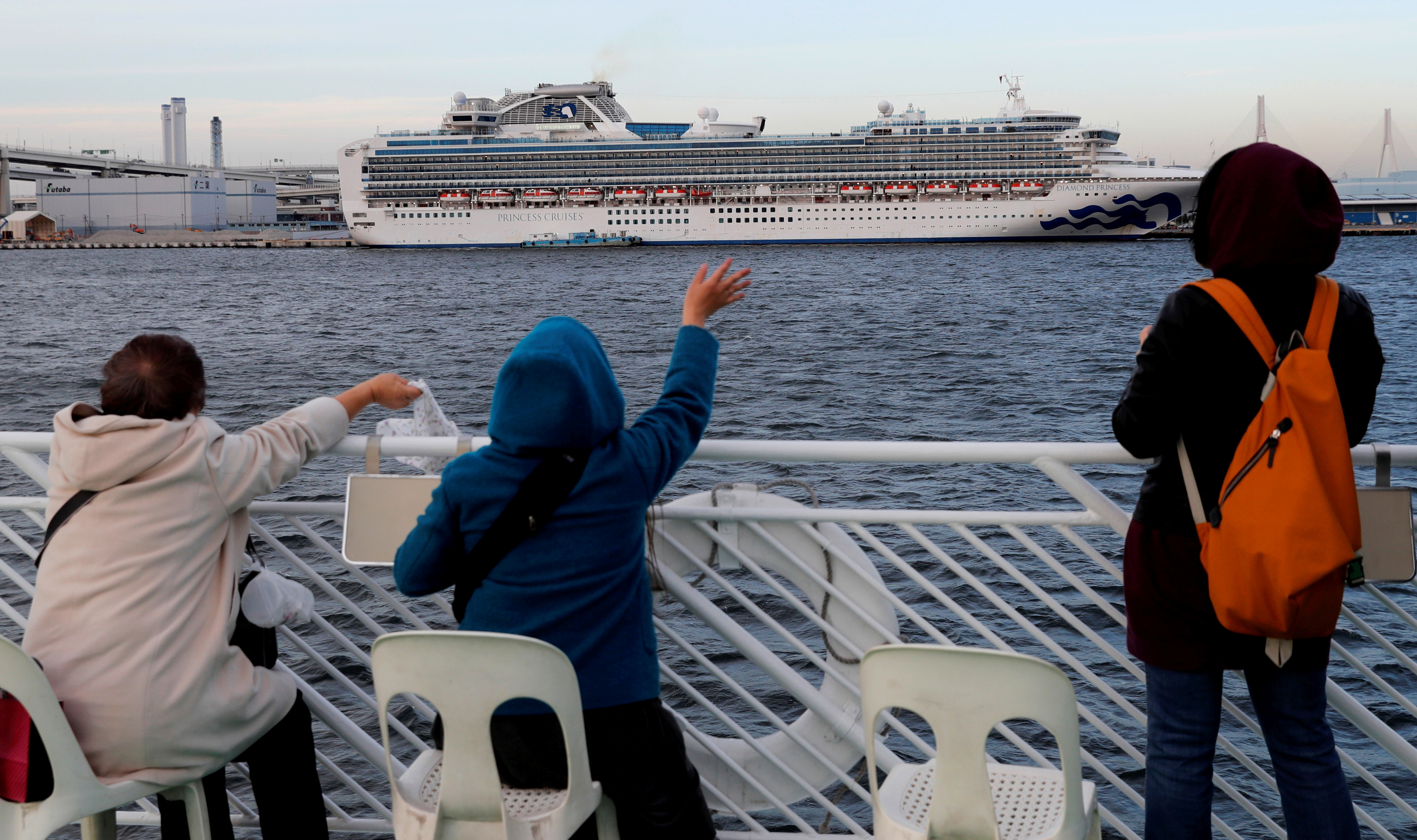 Tourists on a sightseeing cruise ship wave to passengers of the cruise ship Diamond Princess, which is anchored at Daikoku Pier Cruise Terminal in Yokohama