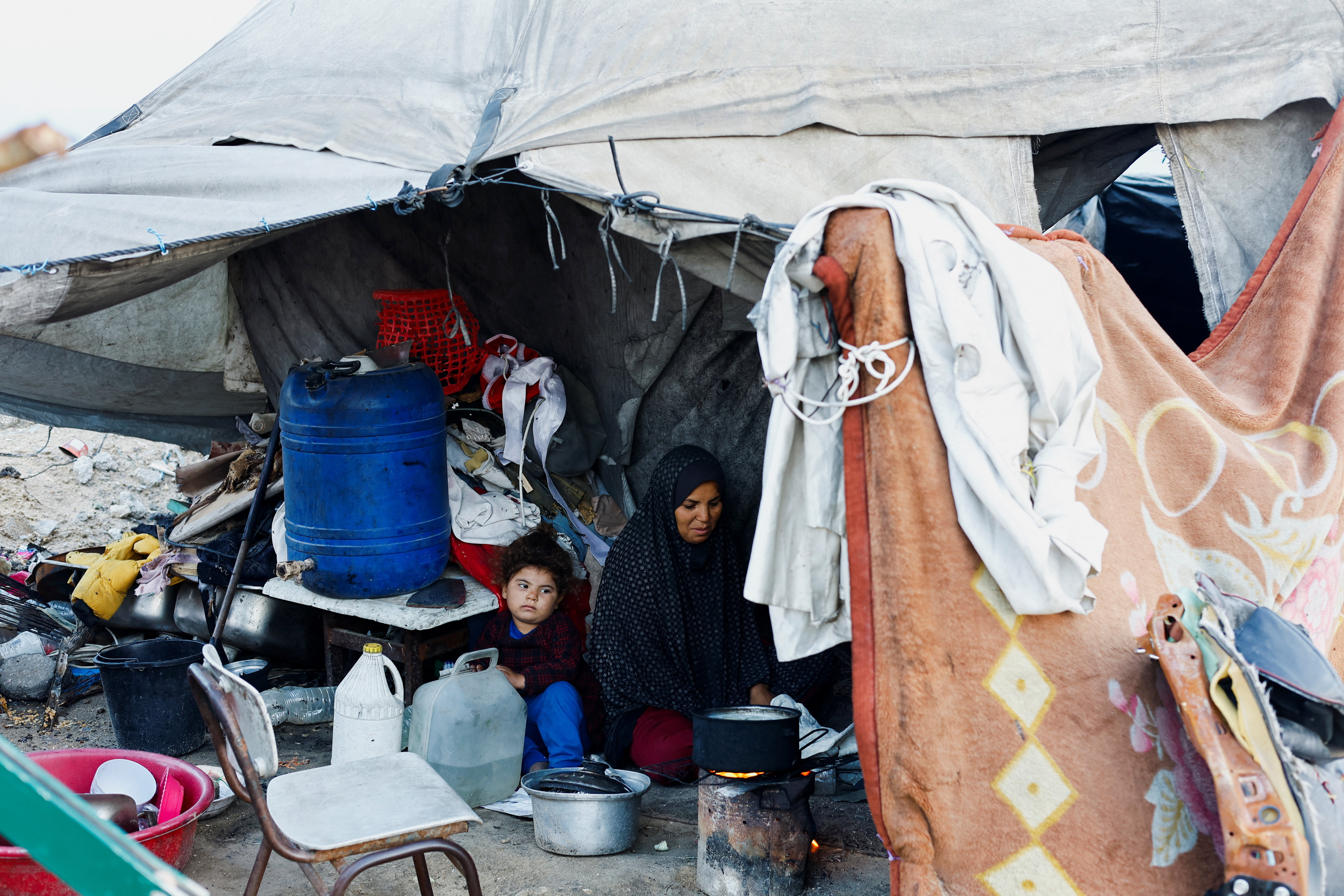 A Palestinian family prepares food over a fire stove in front of their tent in a camp on a rainy day in Nuseirat
