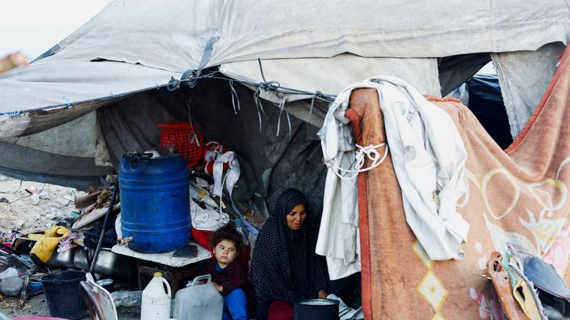 A Palestinian family prepares food over a fire stove in front of their tent in a camp on a rainy day in Nuseirat