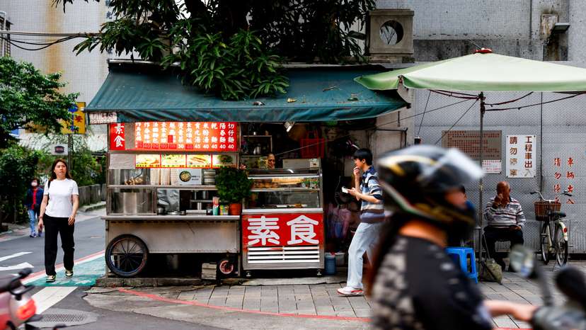 People walk near a food stall on a corner of a street in Taipei