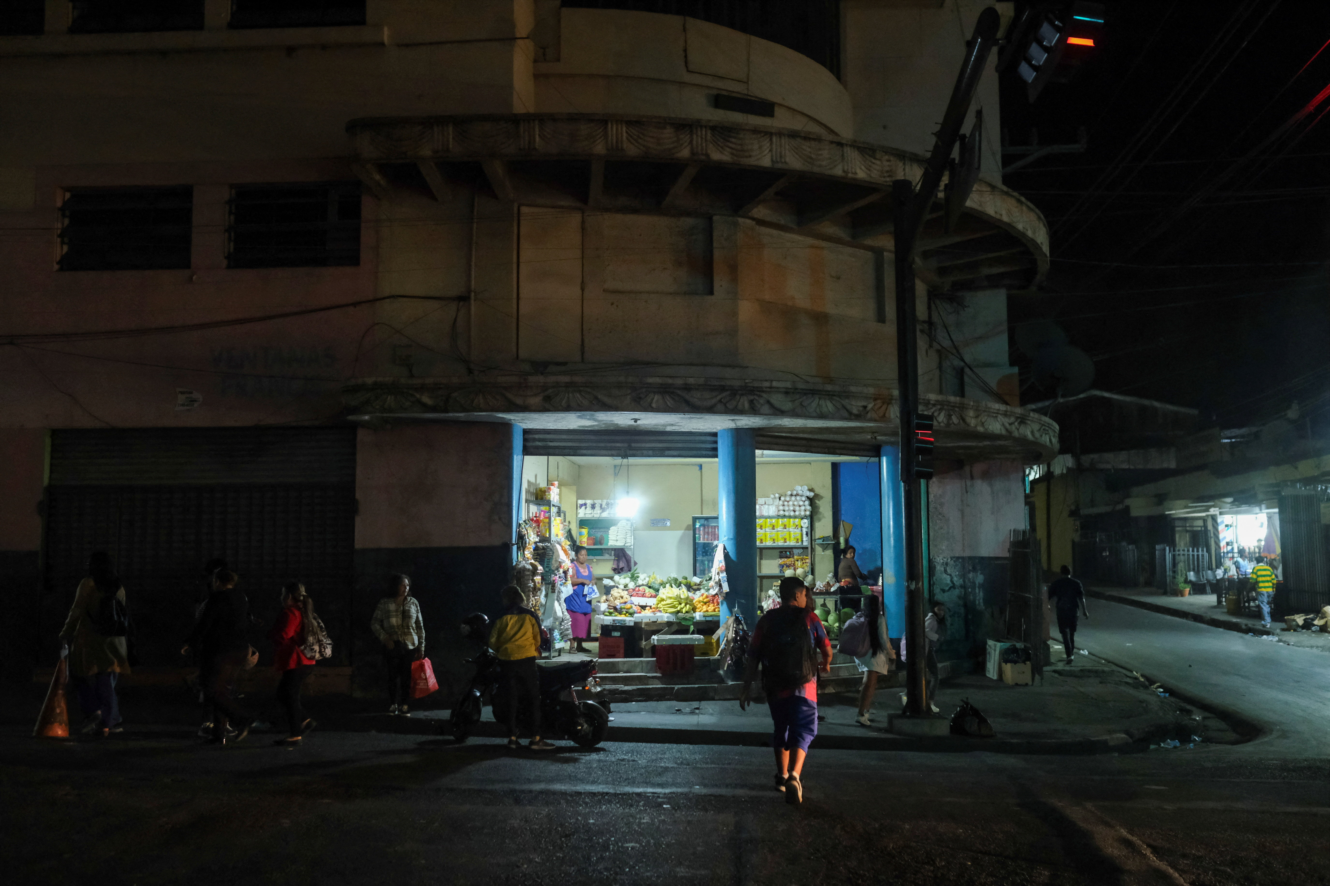 People wait for a bus by a produce store in downtown San Salvador