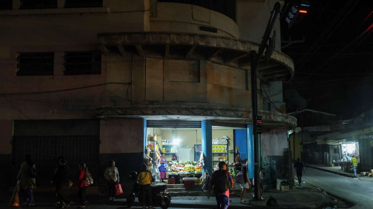 People wait for a bus by a produce store in downtown San Salvador