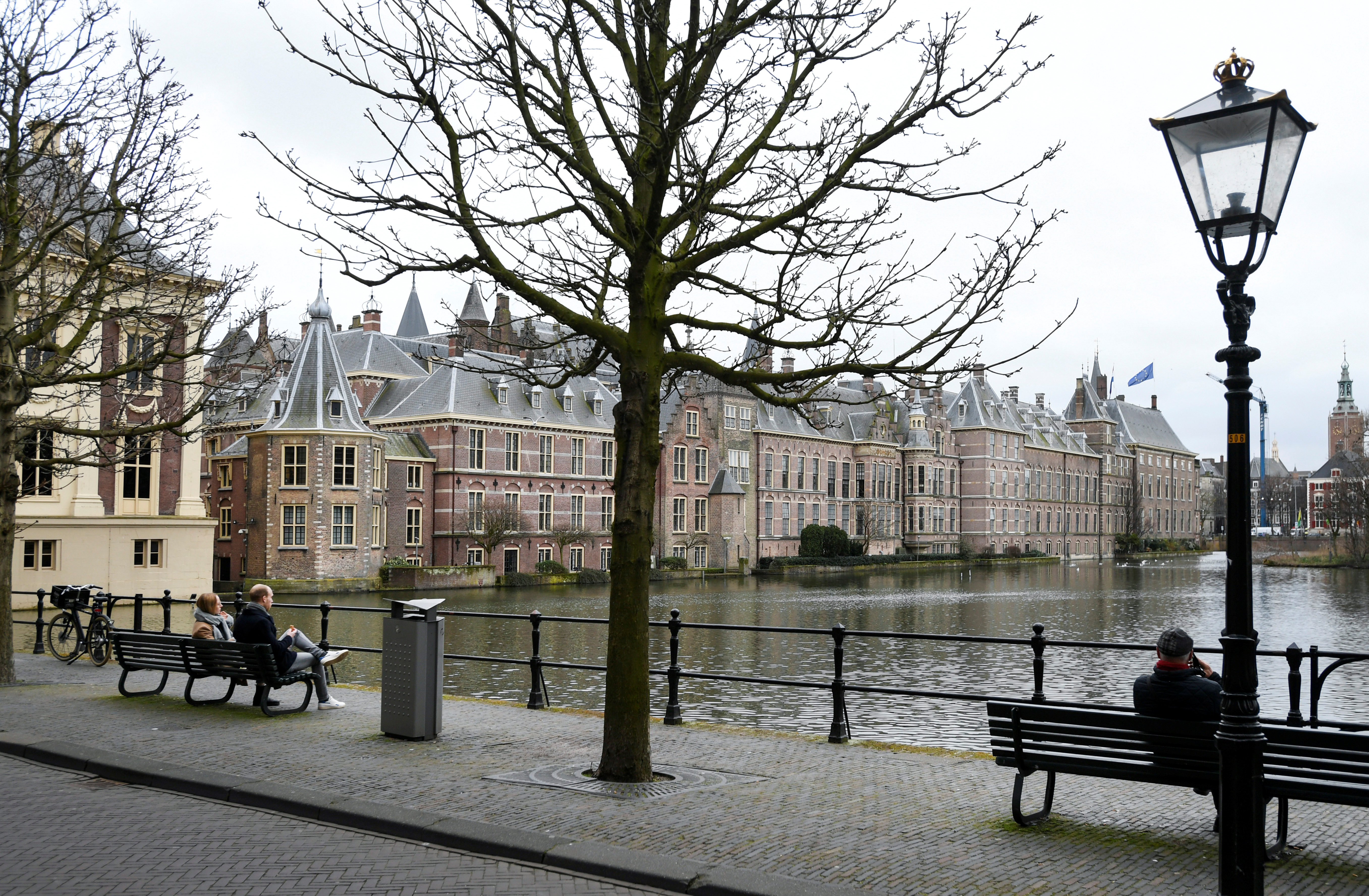 People sit on benches with a view of the parliament building in The Hague