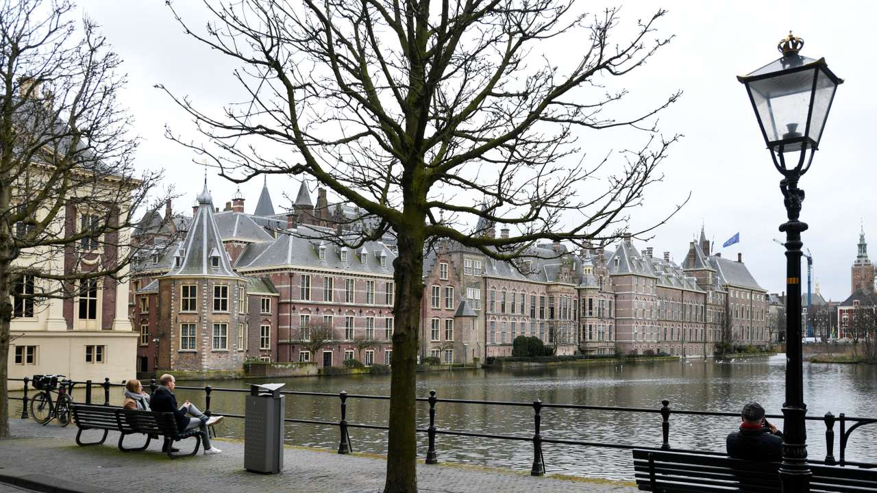 People sit on benches with a view of the parliament building in The Hague
