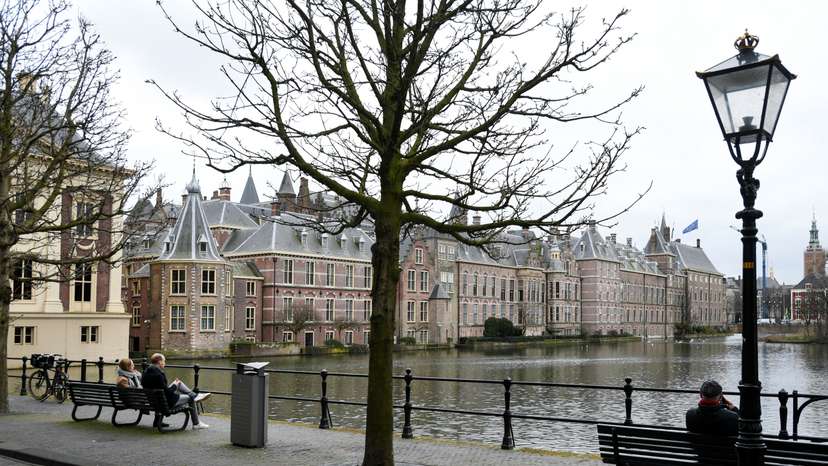People sit on benches with a view of the parliament building in The Hague