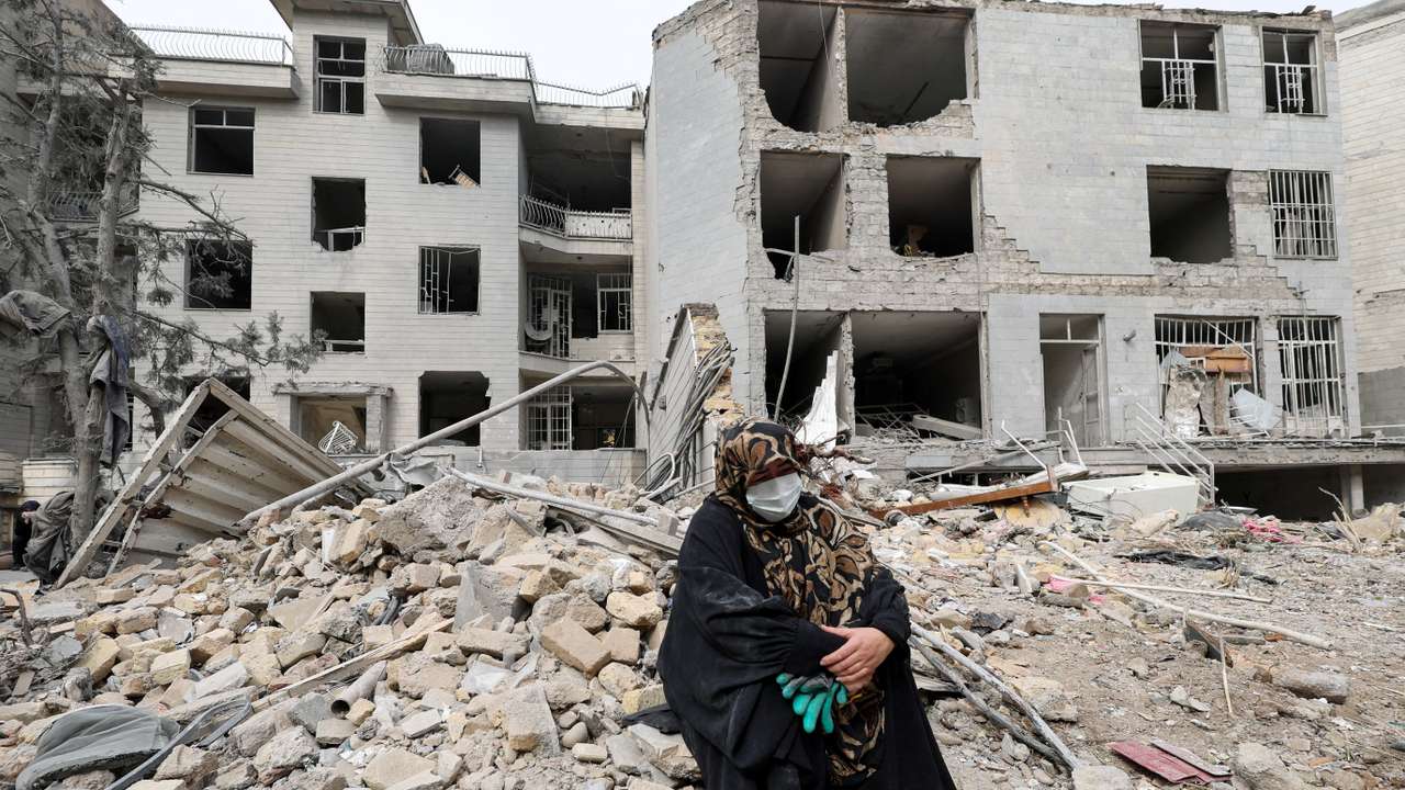 A woman sits outside her destroyed apartment after it was damaged, in Tehran
