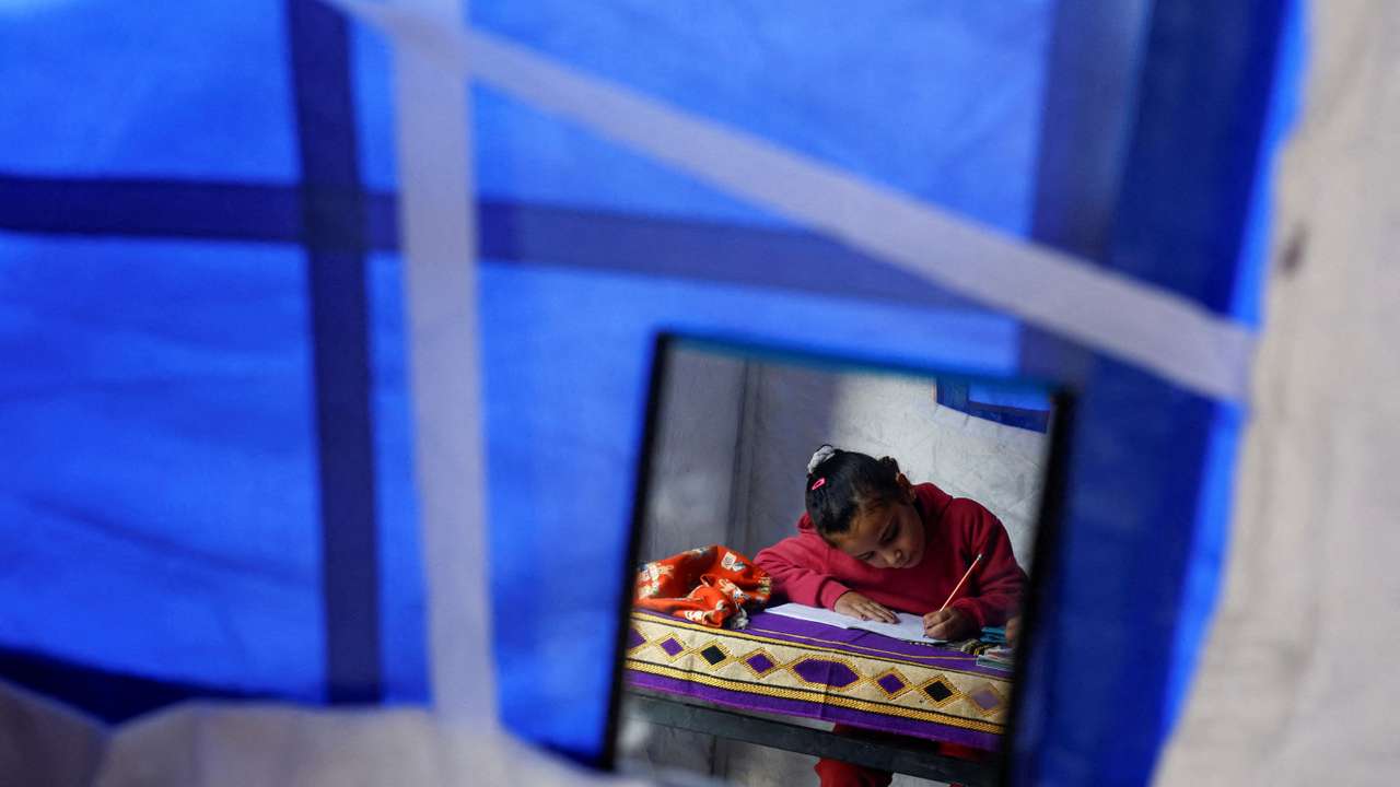 Displaced Palestinian girl Toulin Al-Hindi, is reflected in a hanging mirror as she does her homework inside her family's tent near the Israeli-designated "yellow line" in Beit Lahiya
