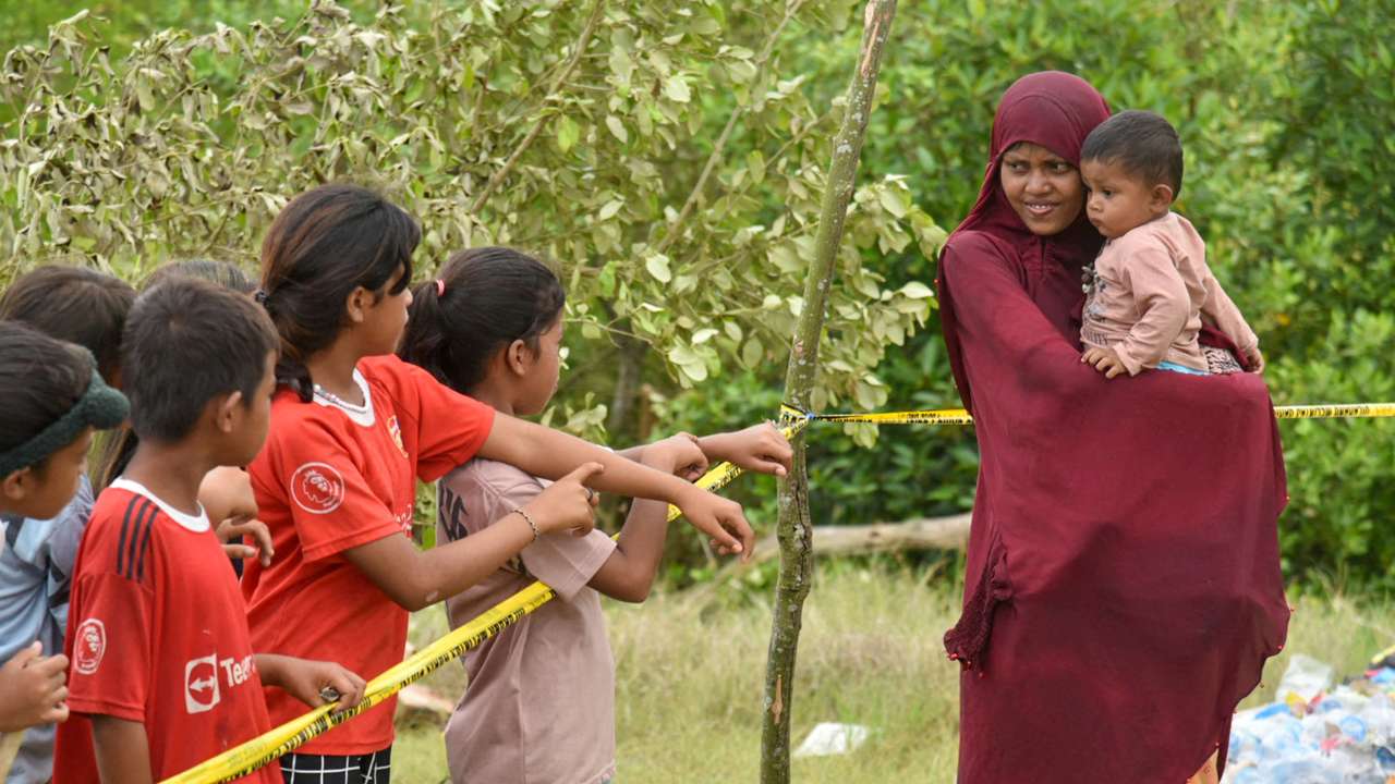 A Rohingya Muslim woman carries her child as she greets locals at a temporary shelter, following their arrival in Karang Gading village