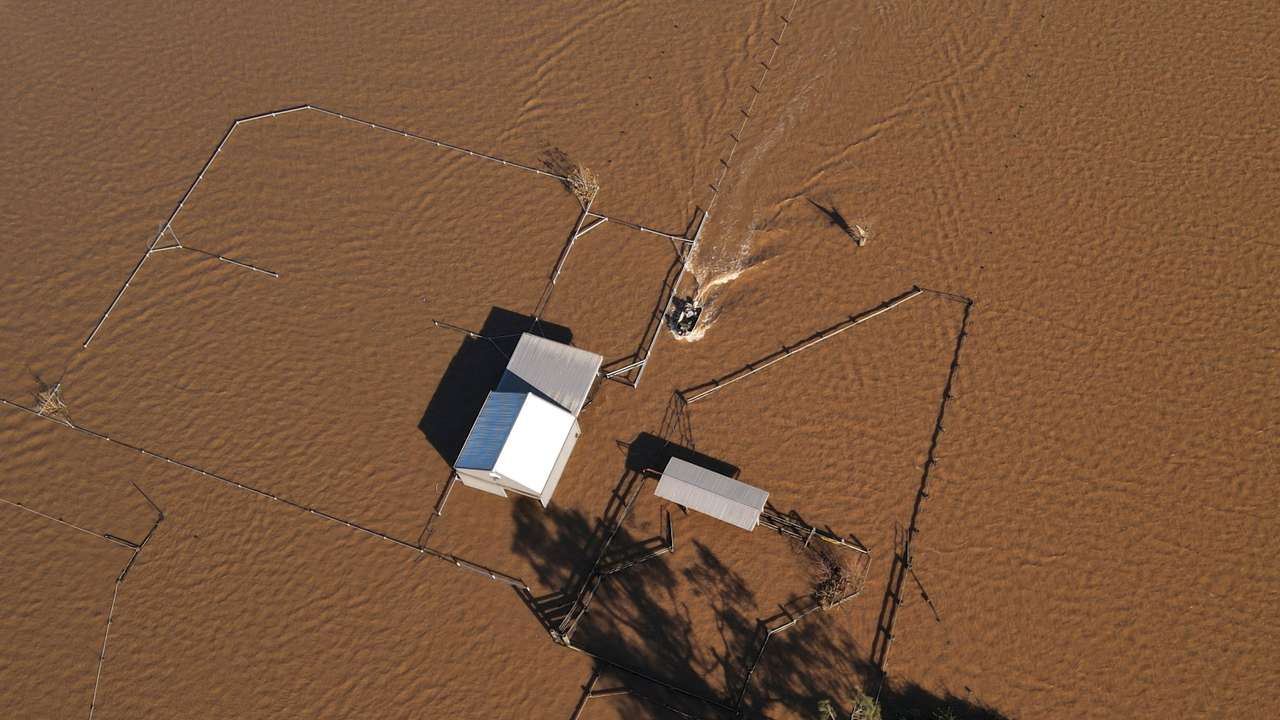 A drone view shows a boat approaching a flooded shed at a stud farm in Heatherbrae