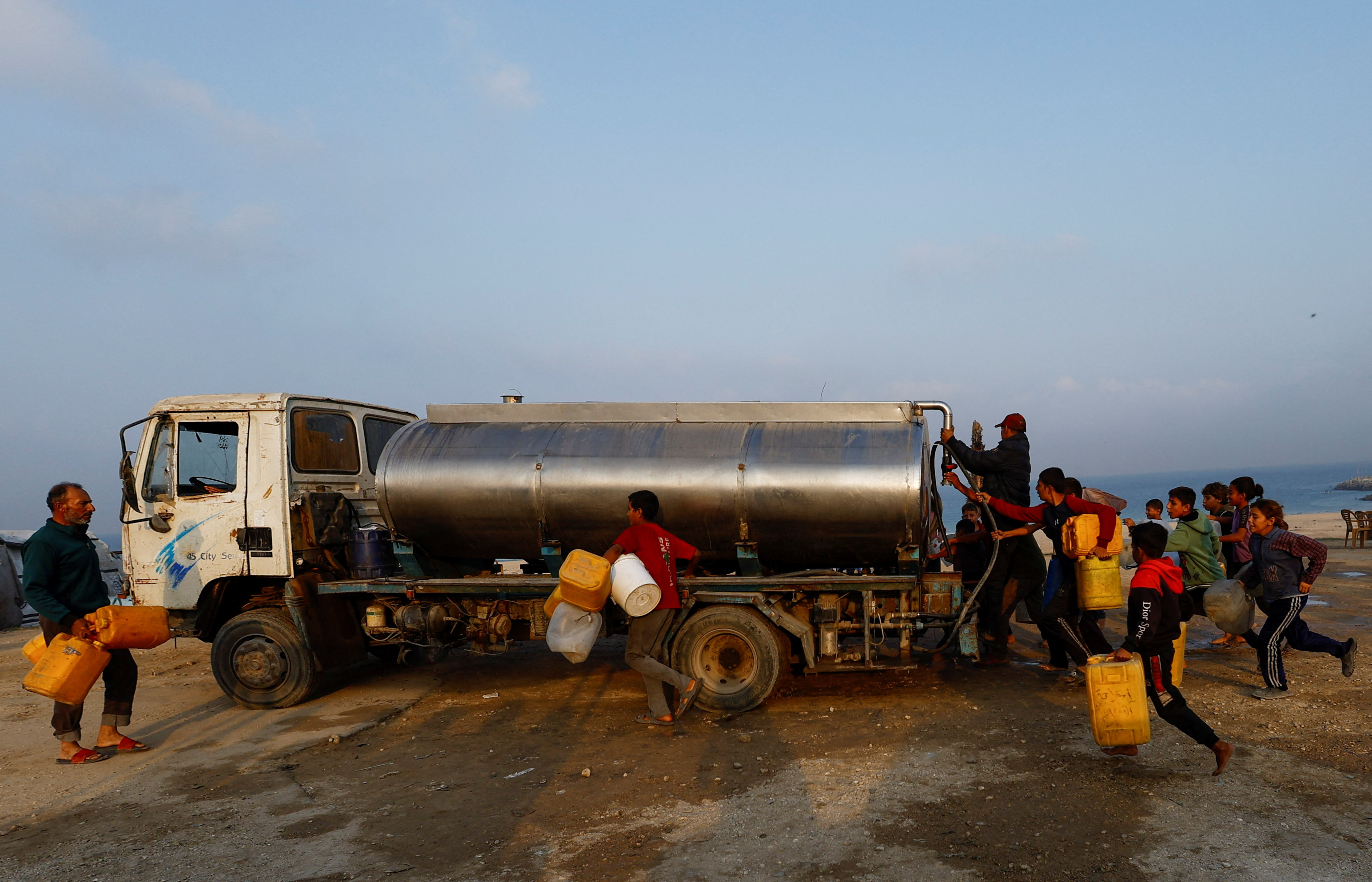 Displaced Palestinians run to fill containers with water amid a ceasefire between Israel and Hamas, in Gaza City