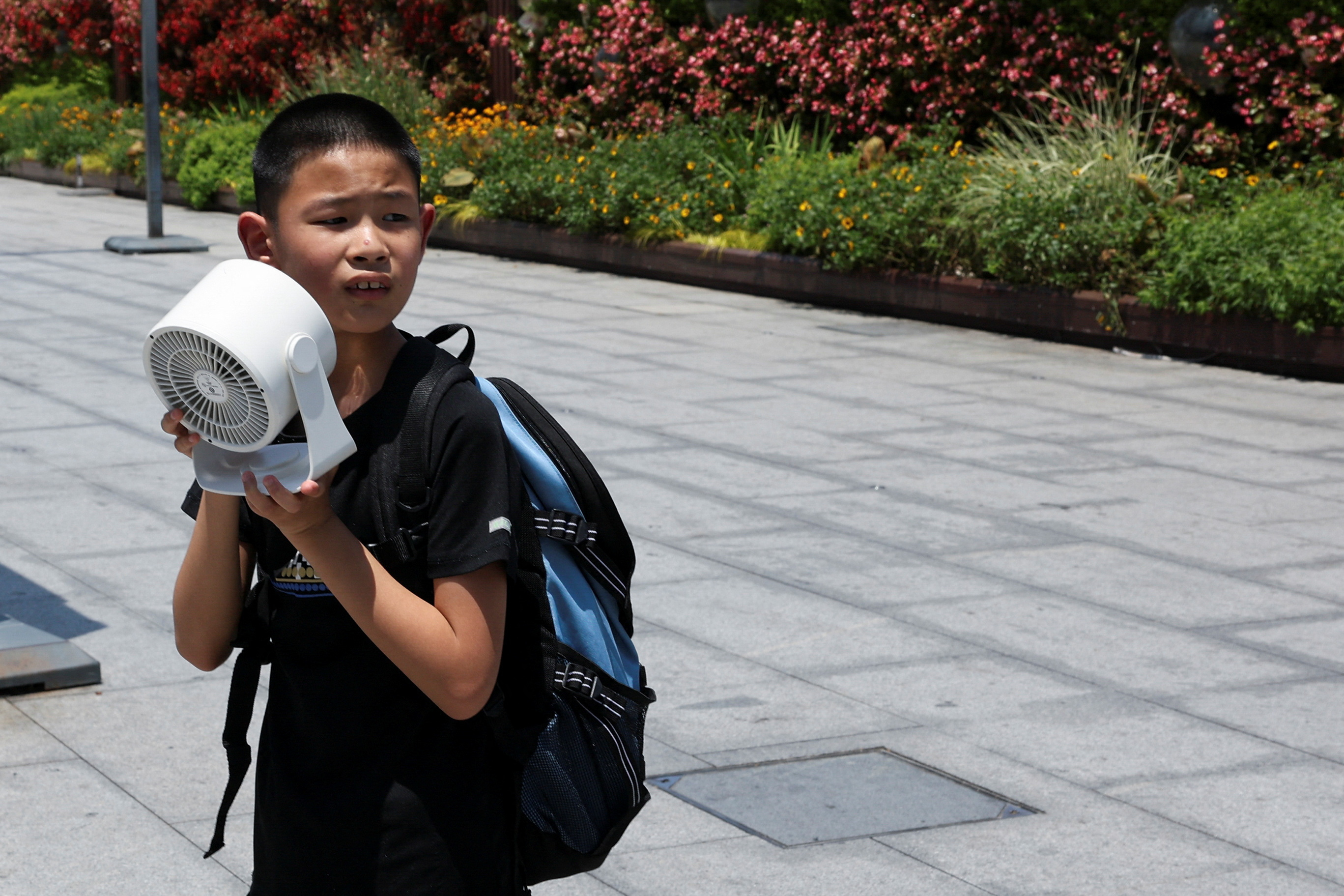 A child holds a portable fan amid a yellow alert for heat, in Shanghai