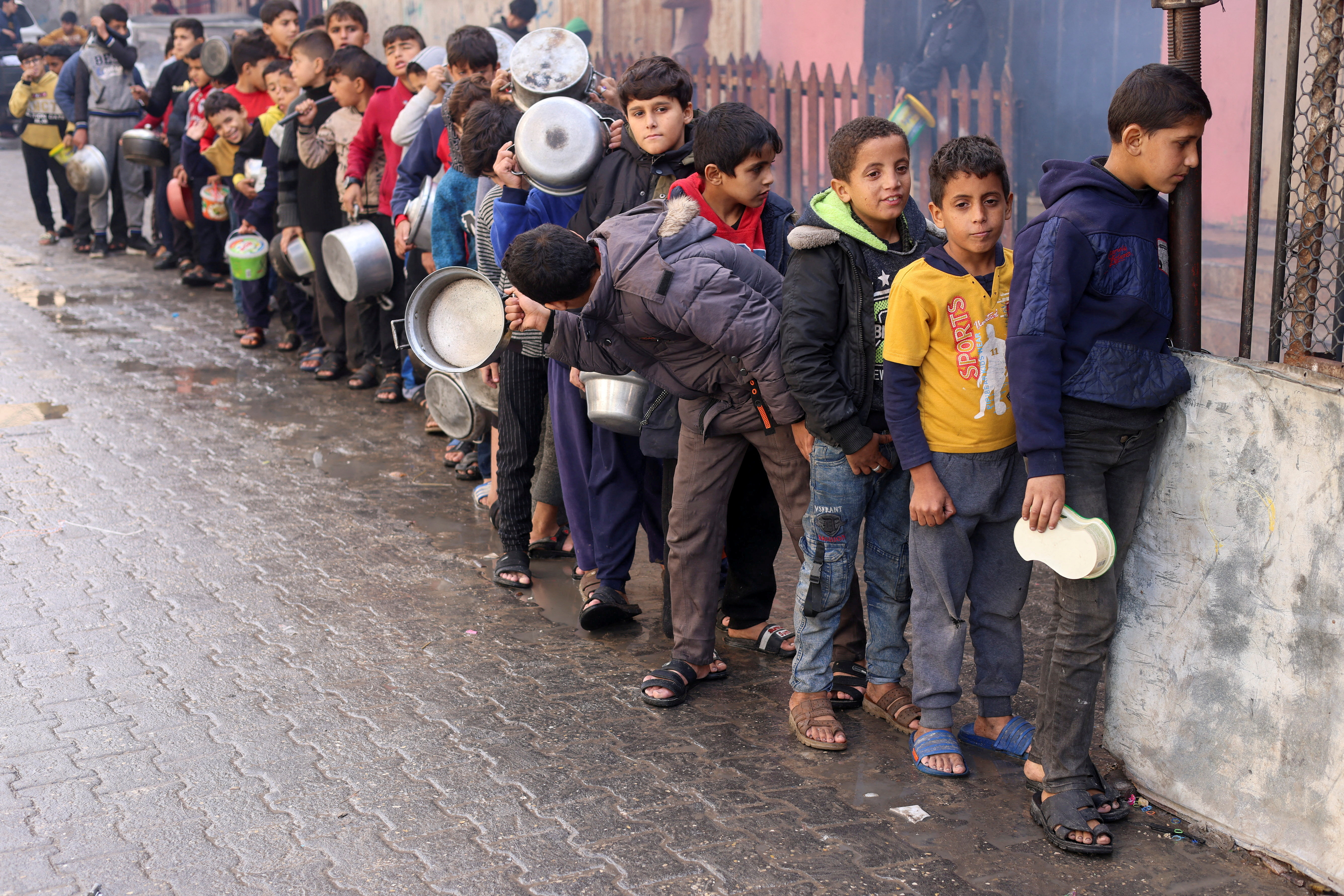 FILE PHOTO: Palestinian children carry pots as they queue to receive food cooked by a charity kitchen, in Rafah in the southern Gaza Strip