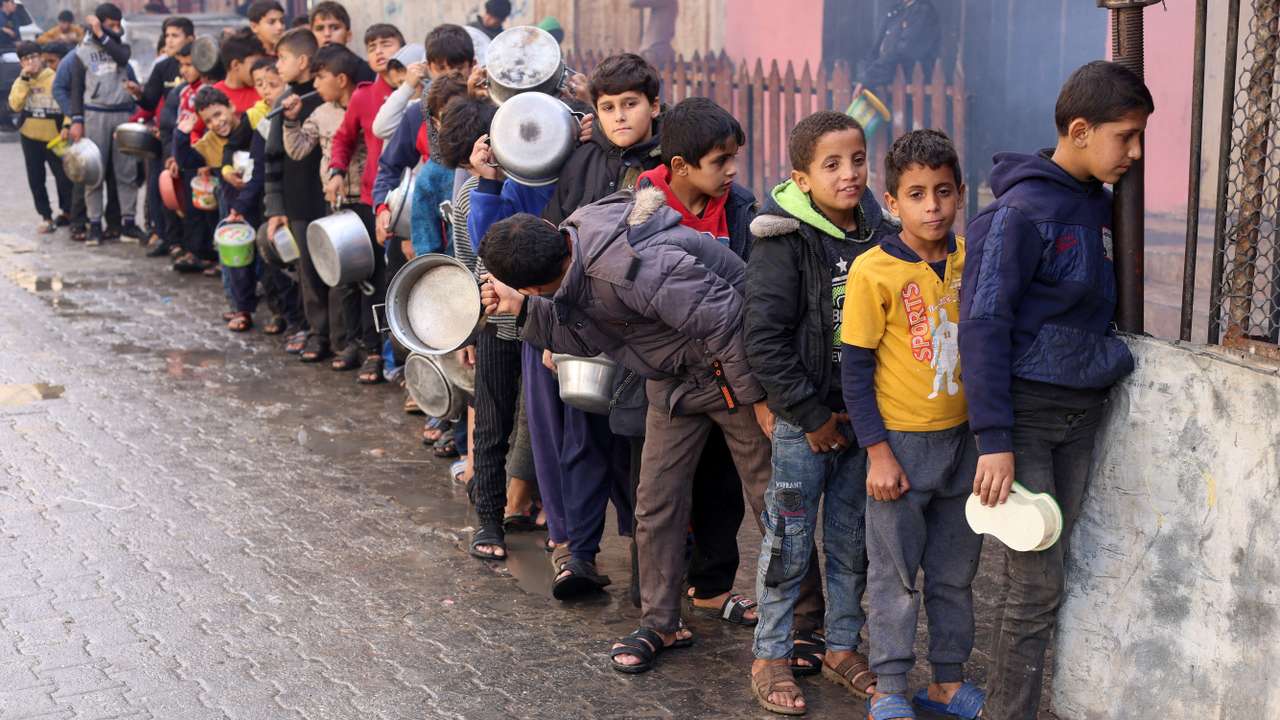 FILE PHOTO: Palestinian children carry pots as they queue to receive food cooked by a charity kitchen, in Rafah in the southern Gaza Strip