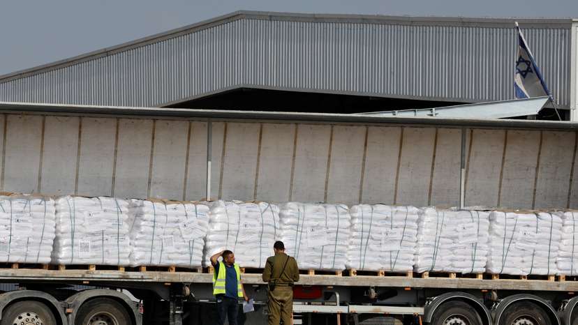 An Israeli security forces member speaks to a worker next to a truck carrying aid at the Kerem Shalom crossing between Israel and Gaza, before going into Gaza, on the Israeli side of the Israel-Gaza border