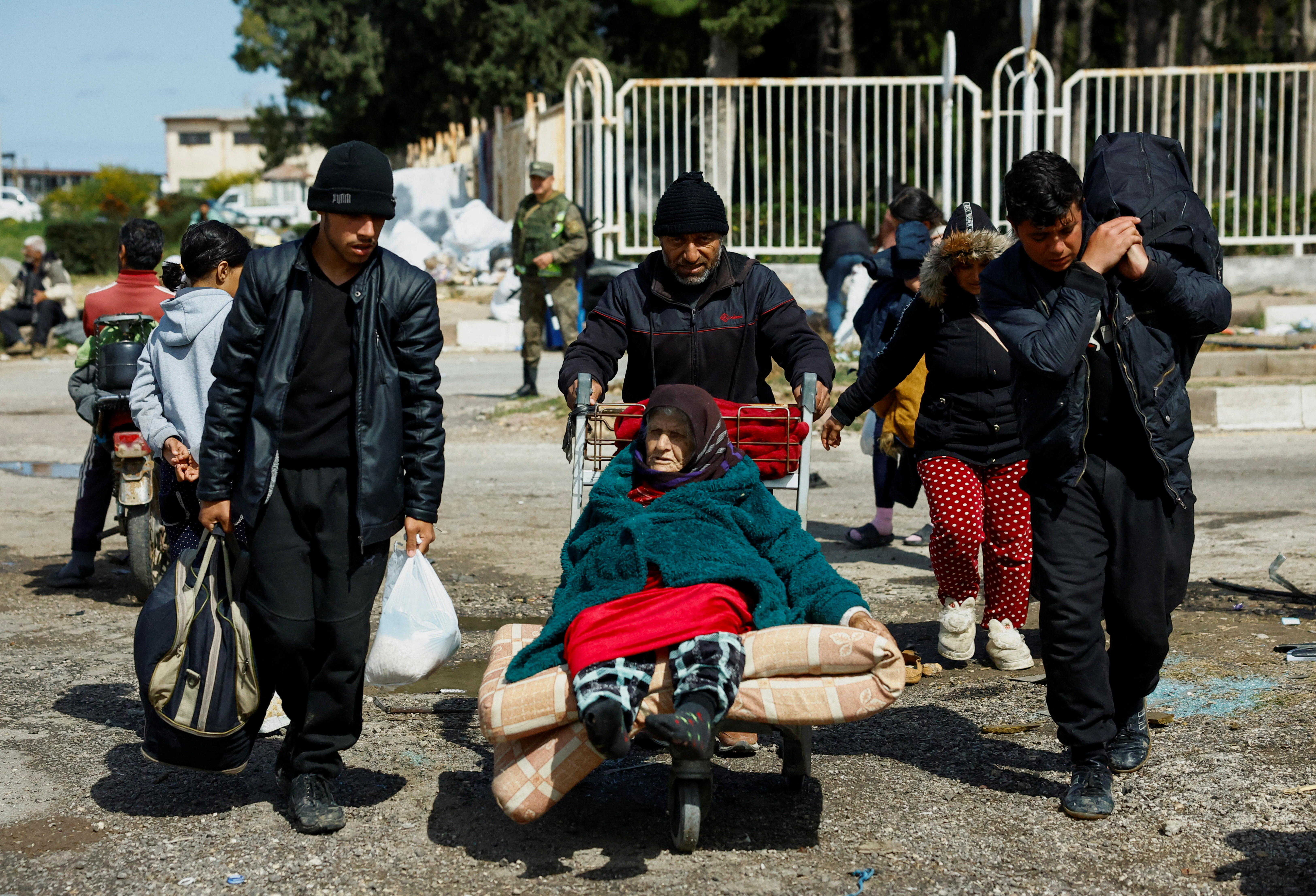 A man pushes an elderly woman on an airport luggage trolley at Hmeimim Air Base, in Latakia