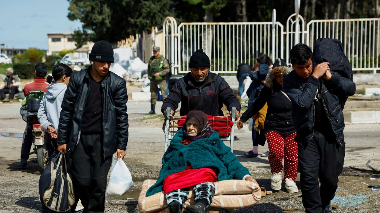 A man pushes an elderly woman on an airport luggage trolley at Hmeimim Air Base, in Latakia