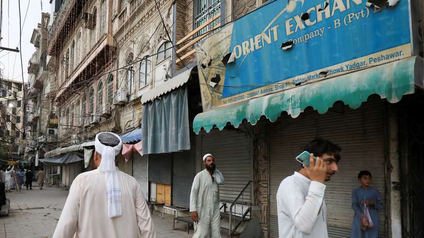 People walk along closed foreign exchange shops, in Peshawar