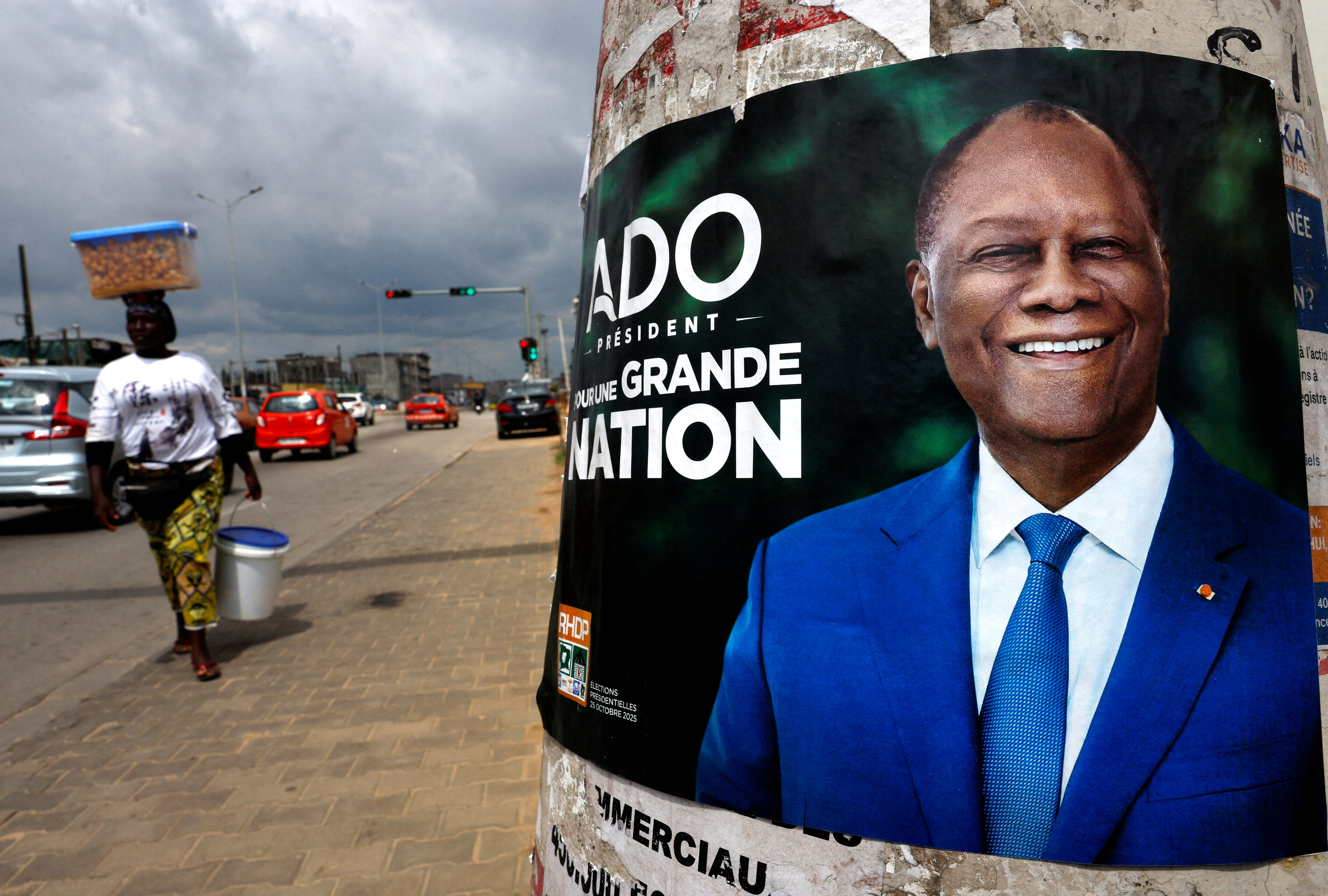 FILE PHOTO: A vendor walks near a campaign poster of Ivory Coast's President Alassane Ouattara, in Abidjan
