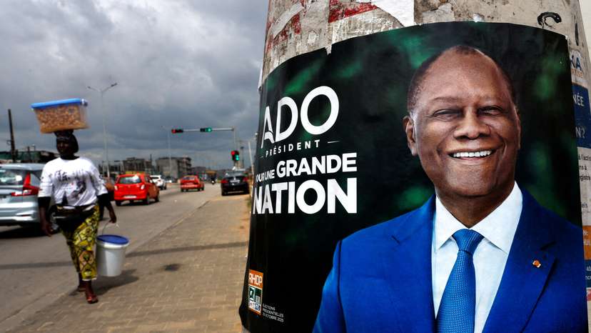 FILE PHOTO: A vendor walks near a campaign poster of Ivory Coast's President Alassane Ouattara, in Abidjan