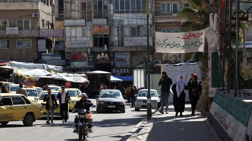 Cars drive and people walk along a street in Sweida