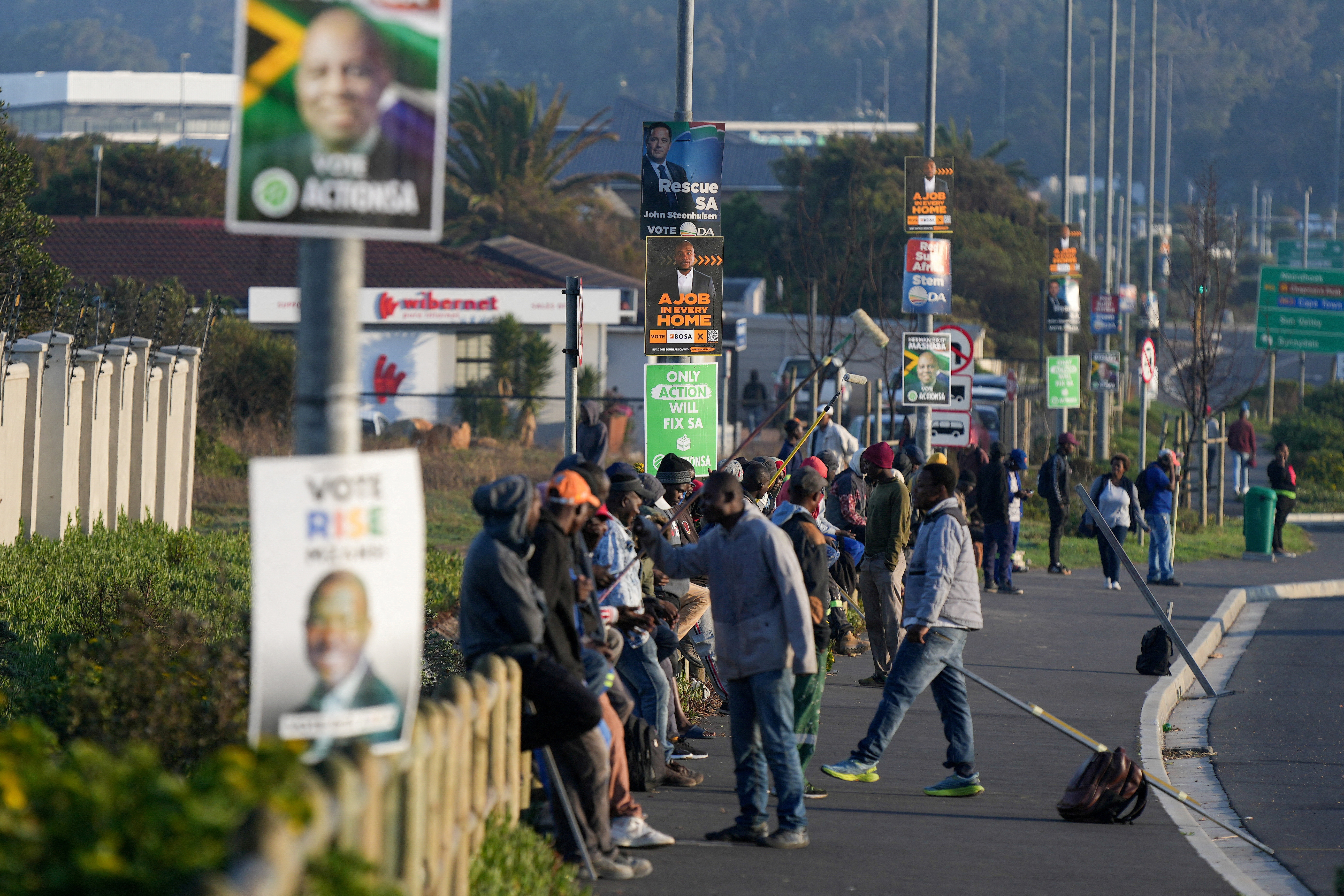 FILE PHOTO: Job seekers sit beneath campaign posters for the South African general elections, in Cape Town