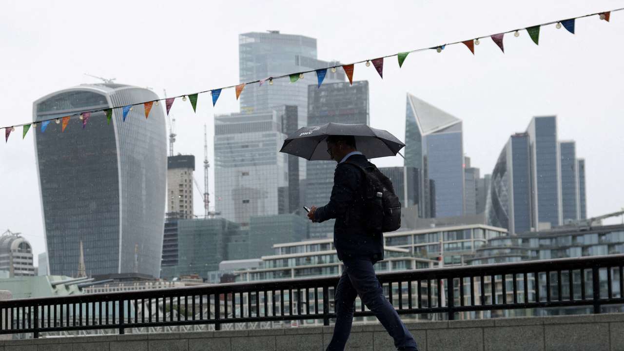FILE PHOTO: A pedestrian carrying an umbrella walks along the River Thames in view of City of London skyline in London