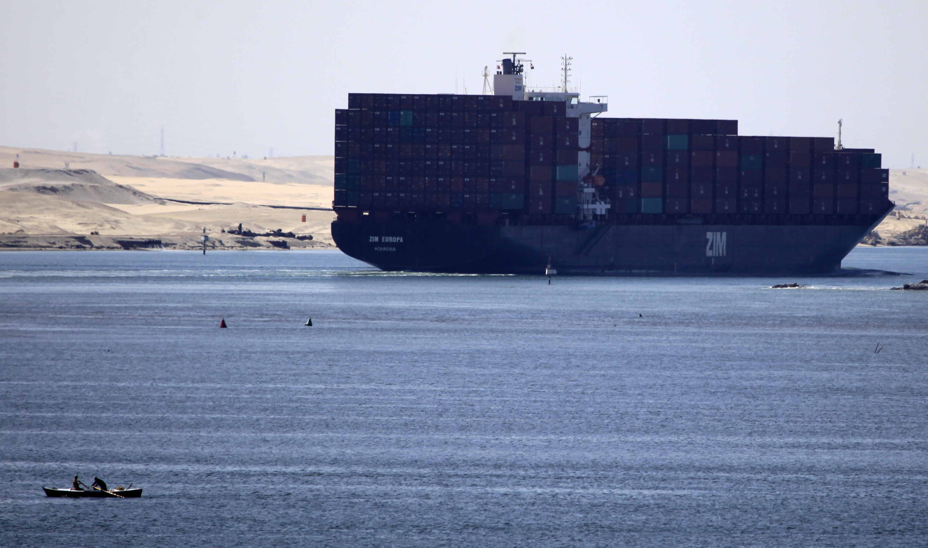 A fisherman travels on a boat with his family in front of the Zim Europa container ship, in the Suez canal