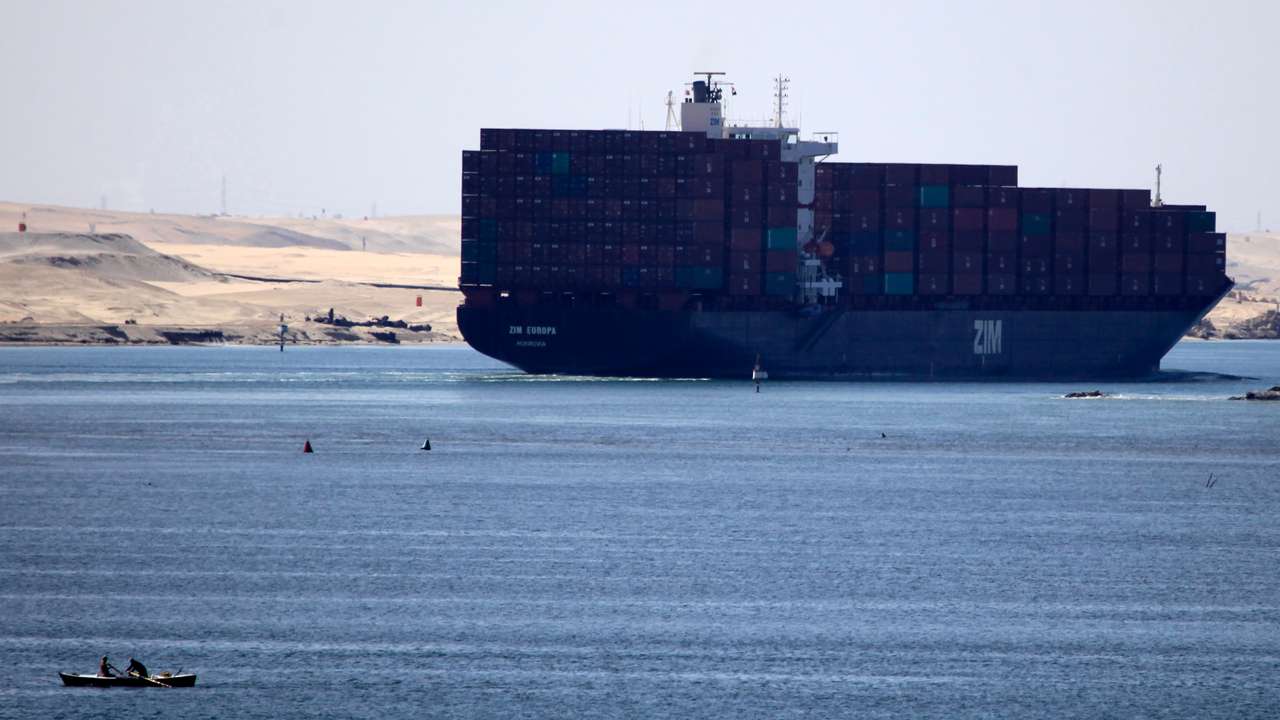 A fisherman travels on a boat with his family in front of the Zim Europa container ship, in the Suez canal