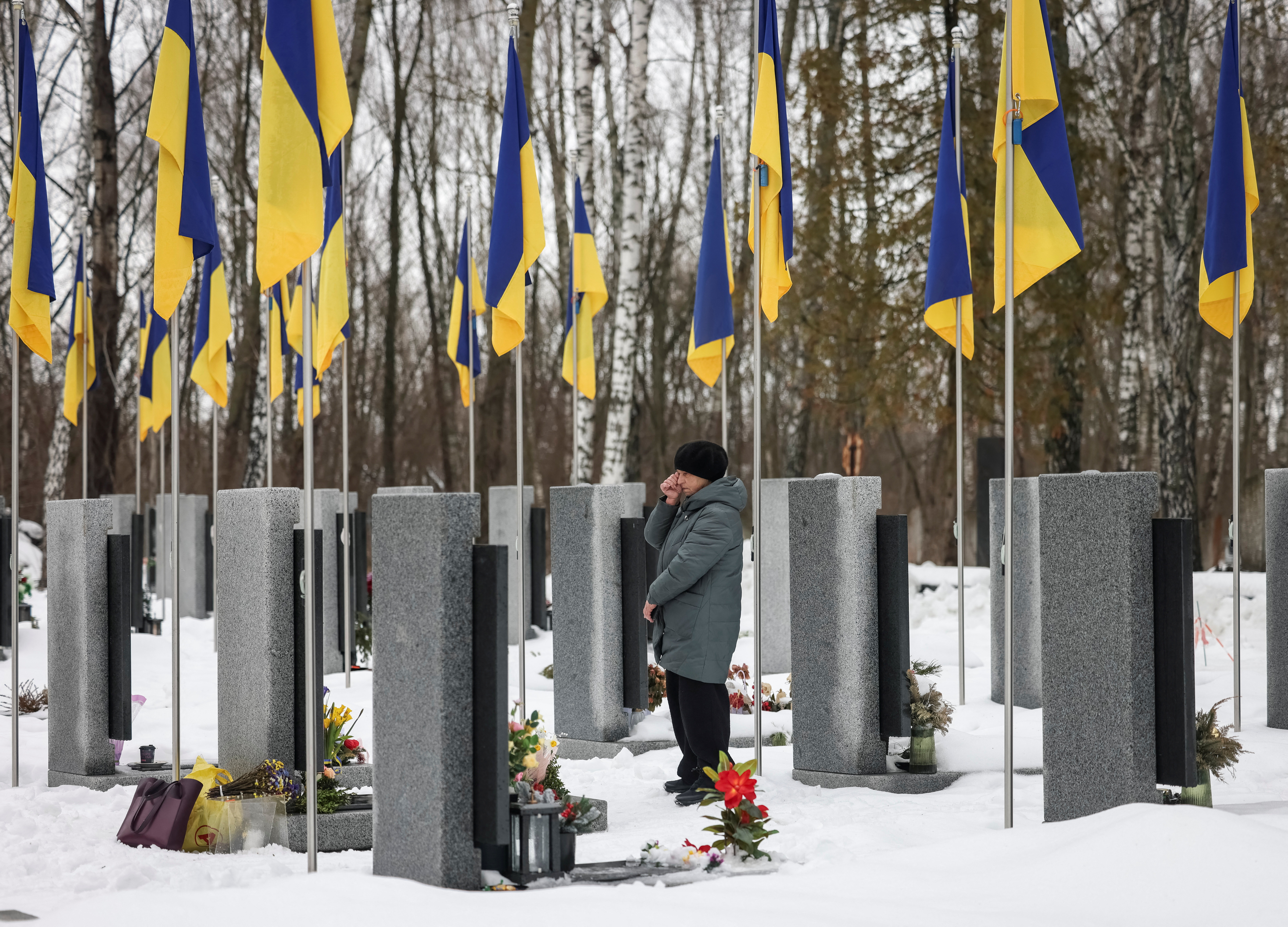 A woman reacts as she stands in front of a grave at a local cemetery, as she pays tribute to the victims of the Russian attack on Ukraine