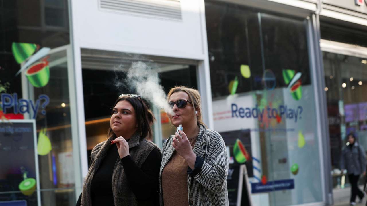 A woman holds an e-cigarette as she vapes on a street in Manchester
