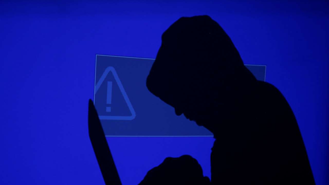 FILE PHOTO: Hooded man holds laptop computer as blue screen with an exclamation mark is projected on him in this illustration picture