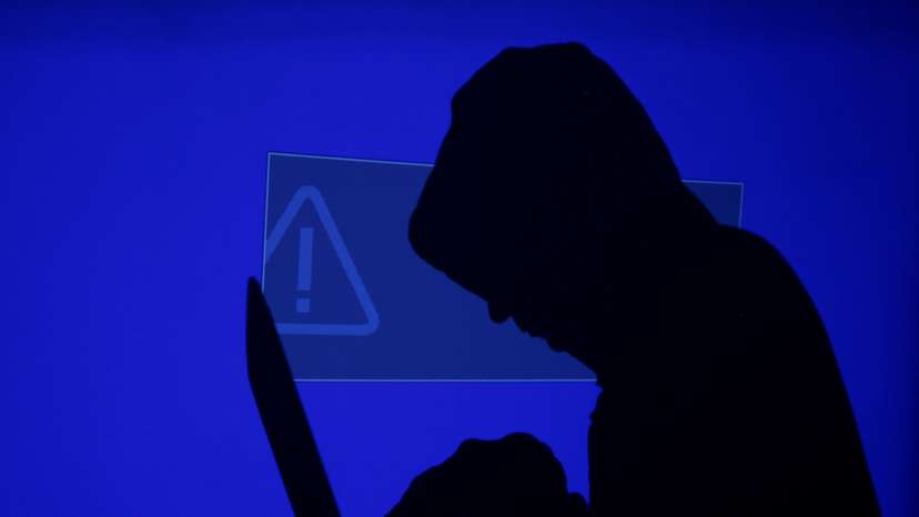 FILE PHOTO: Hooded man holds laptop computer as blue screen with an exclamation mark is projected on him in this illustration picture
