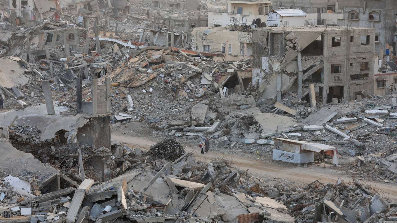 Palestinian women walk among piles of rubble and damaged buildings in Gaza City