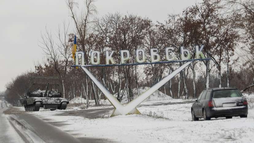 A Ukrainian tank and a car are parked near a road sign that reads, 'Pokrovsk’ in the town of Pokrovsk