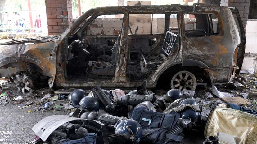 Damaged riot gear of security forces is seen next to a burnt vehicle outside a police station, in Dhaka