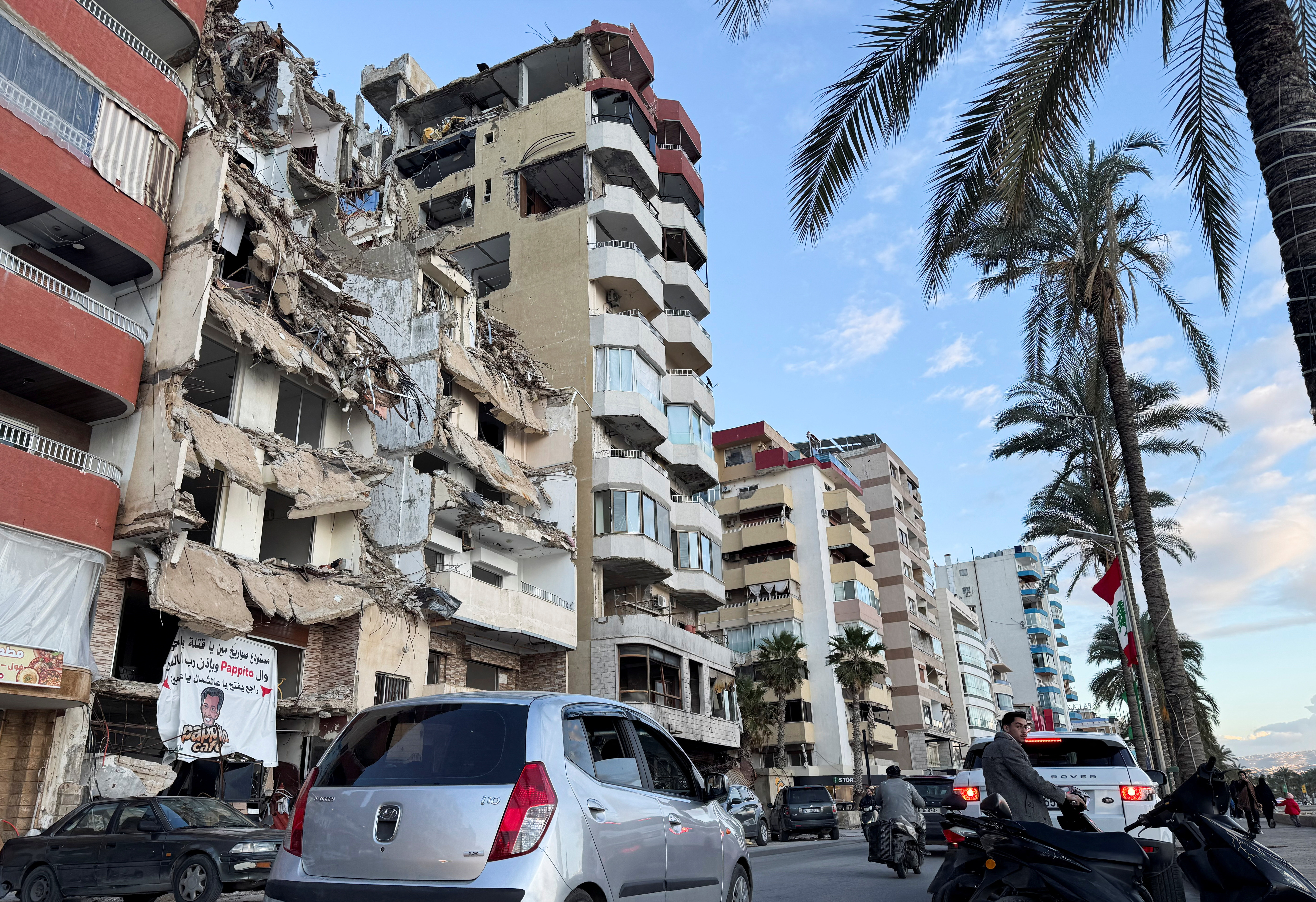 Cars drive past a damaged building near the Corniche, in Tyre