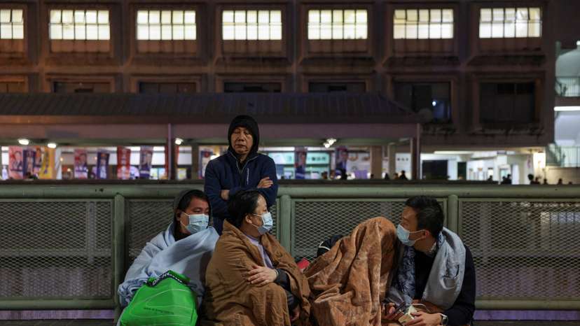 Evacuees wrapped in blankets rest on a nearby platform after a major fire at Wang Fuk Court housing estate, in Tai Po, Hong Kong