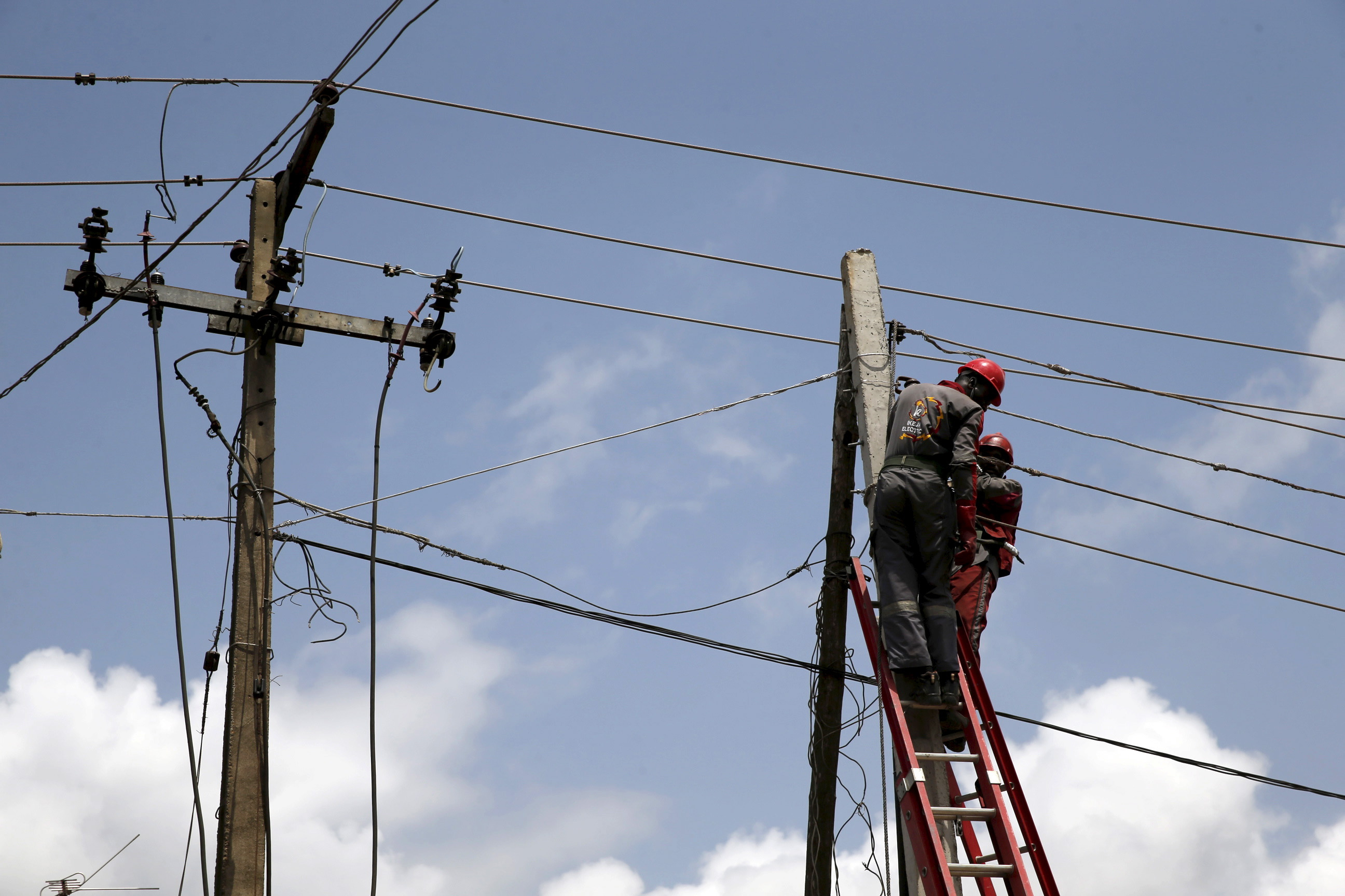 Power officials stand on ladders to fix electric cables along a road in Egbeda dstrict in Lagos