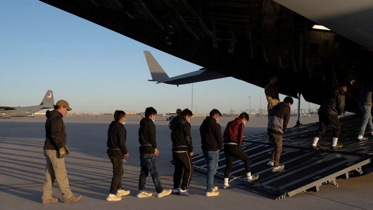 U.S. Customs and Border Protection security agents guide a group of detained migrants to board a removal flight