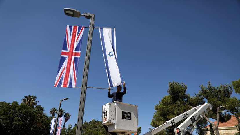 A Jerusalem municipality worker hangs an Israeli flag next to the British flag, the Union Jack, as he stands on a platform near Israel's presidential residence in Jerusalem ahead of the upcoming visit of Britain's Prince William