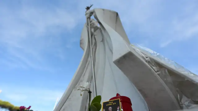 Uma foto do Papa Leão XIV é colocada junto à estátua de João Paulo II, em frente ao Hospital Universitário Gemelli, onde o Papa Leão XIV se recupera após uma cirurgia para remover um tumor cancerígeno do pulmão direito, em Roma.